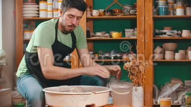 陶器-主人正在用一桶水润湿他的手，并继续用粘土工作